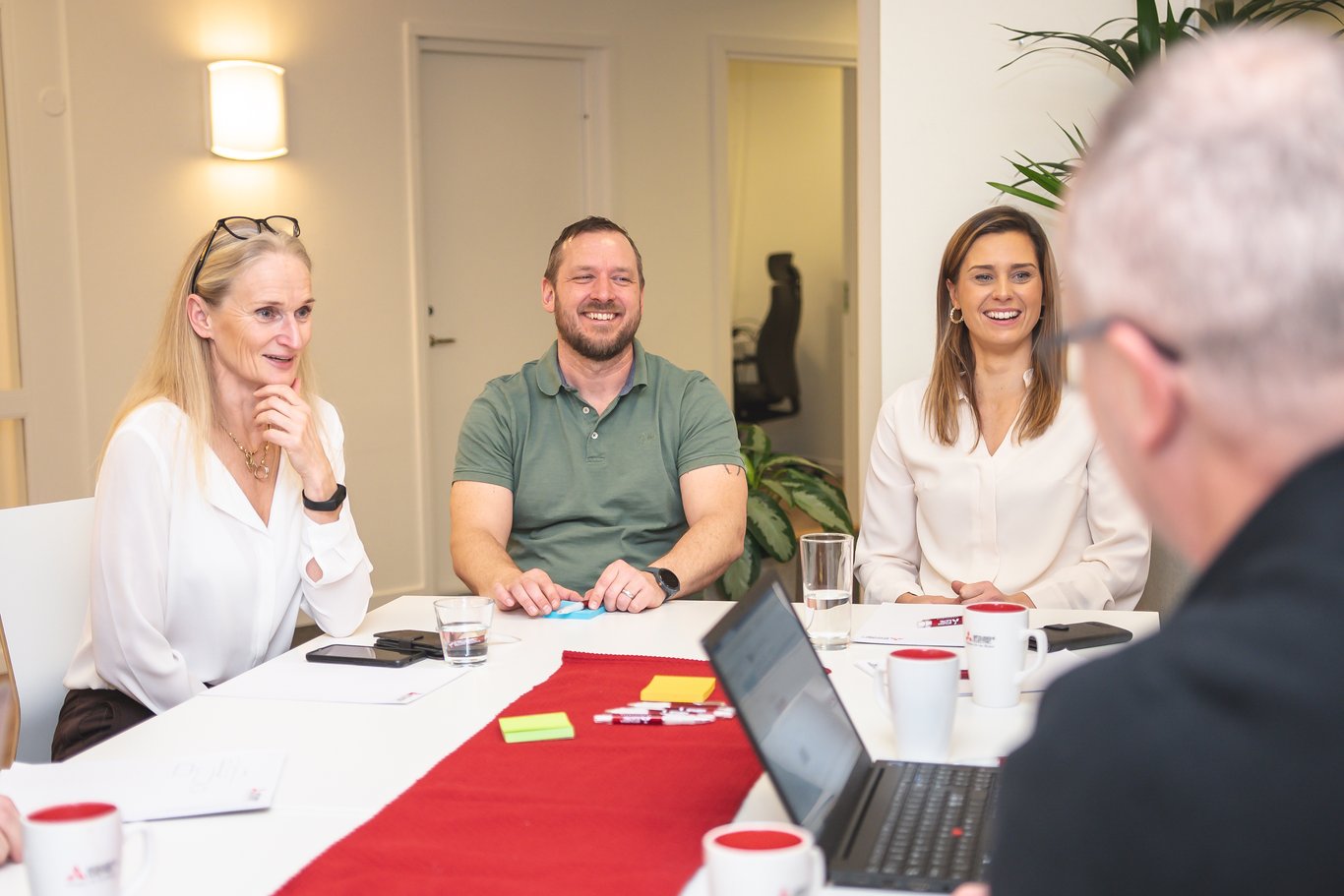 Fyra personer deltar i ett teammöte runt ett bord med dokument och en laptop. En avslappnad atmosfär där Mitsubishi Electric kan bidra med energieffektiva lösningar för kontorsmiljöer.